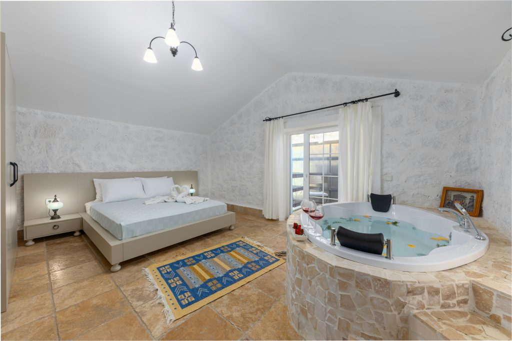 Bedroom suite with a large jacuzzi tub next to the bed, stone floors, soft lighting, and neutral interior design